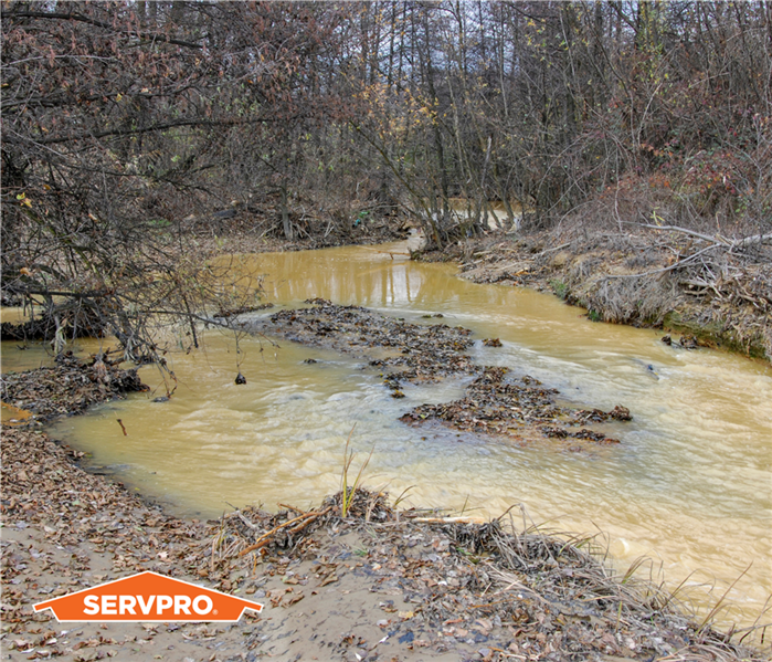 stream after rain filled with muddy water, potential flood water causing water damage, murky brown water, SERVPRO logo