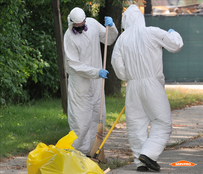 two SERVPRO technicians in white PPE suits and masks cleaning up biohazard materials on a sidewalk